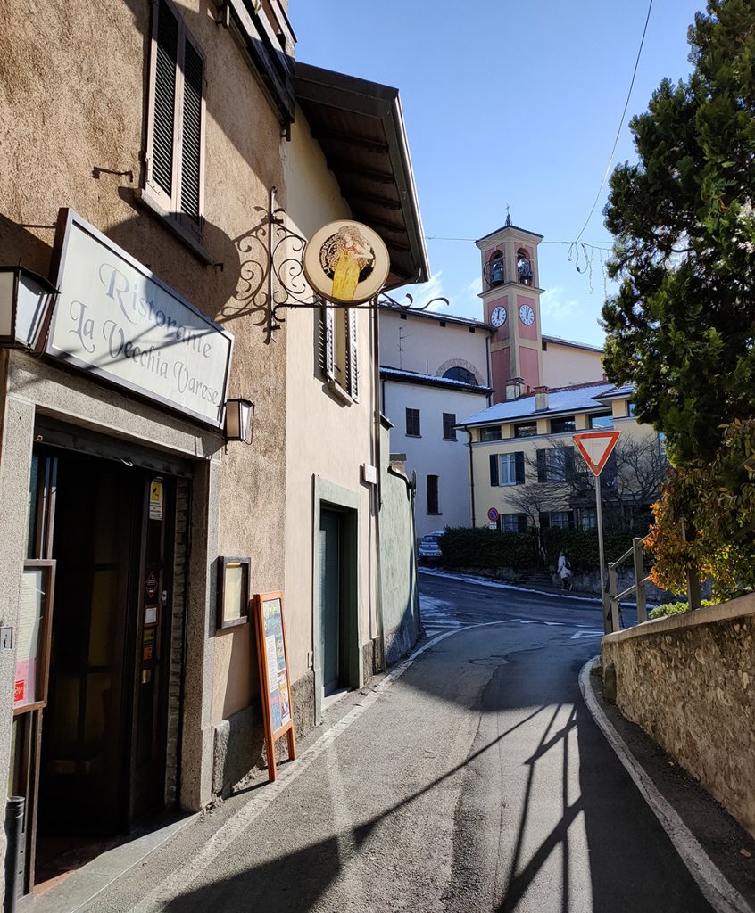 L’ingresso de La Vecchia Varese in Via Ravasi, con l’insegna e il campanile sullo sfondo
